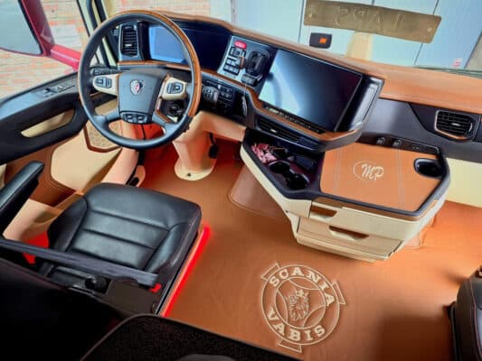 Interiør i lastebil med brunt og sort skinn, tre-detaljer og logoen “Scania Vabis” på gulvet.
