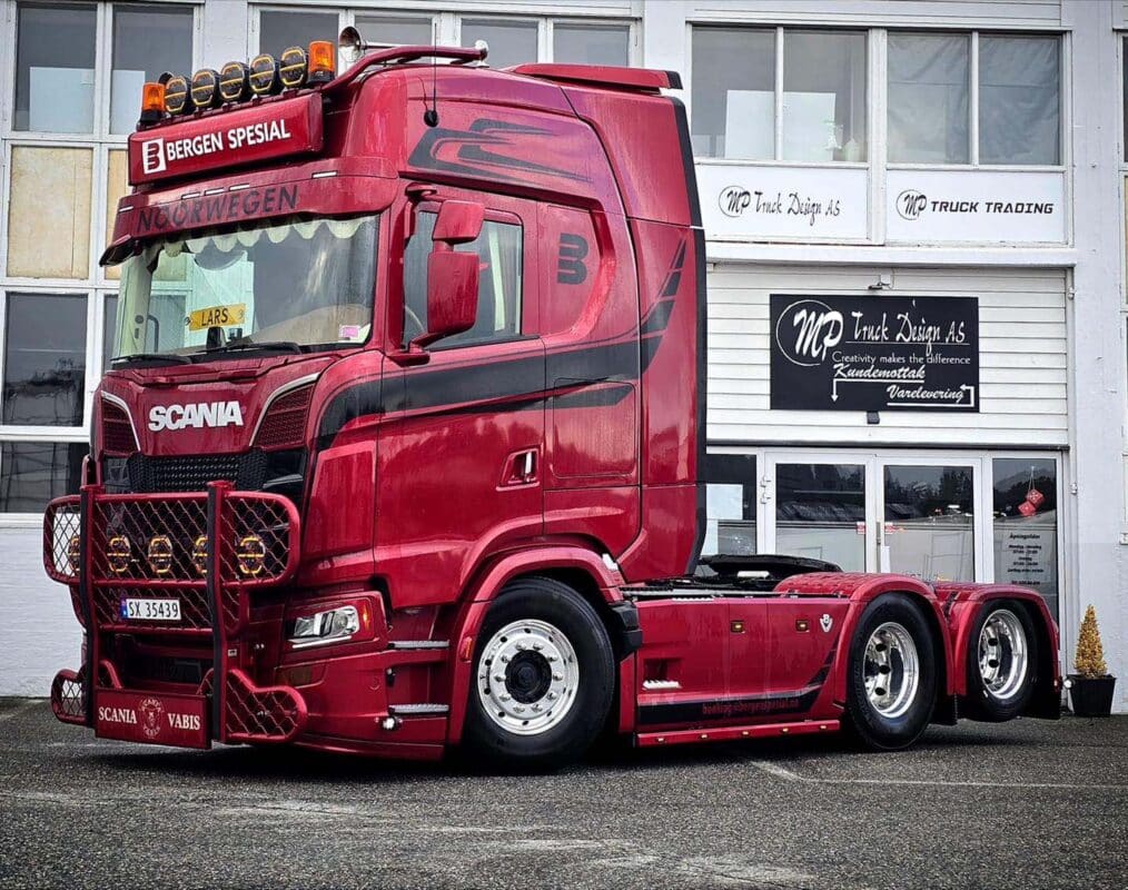 Rød Scania-lastebil parkert foran bygget til MP Truck Design AS, med skiltet “Bergen Spesial” og ekstra lys på taket.