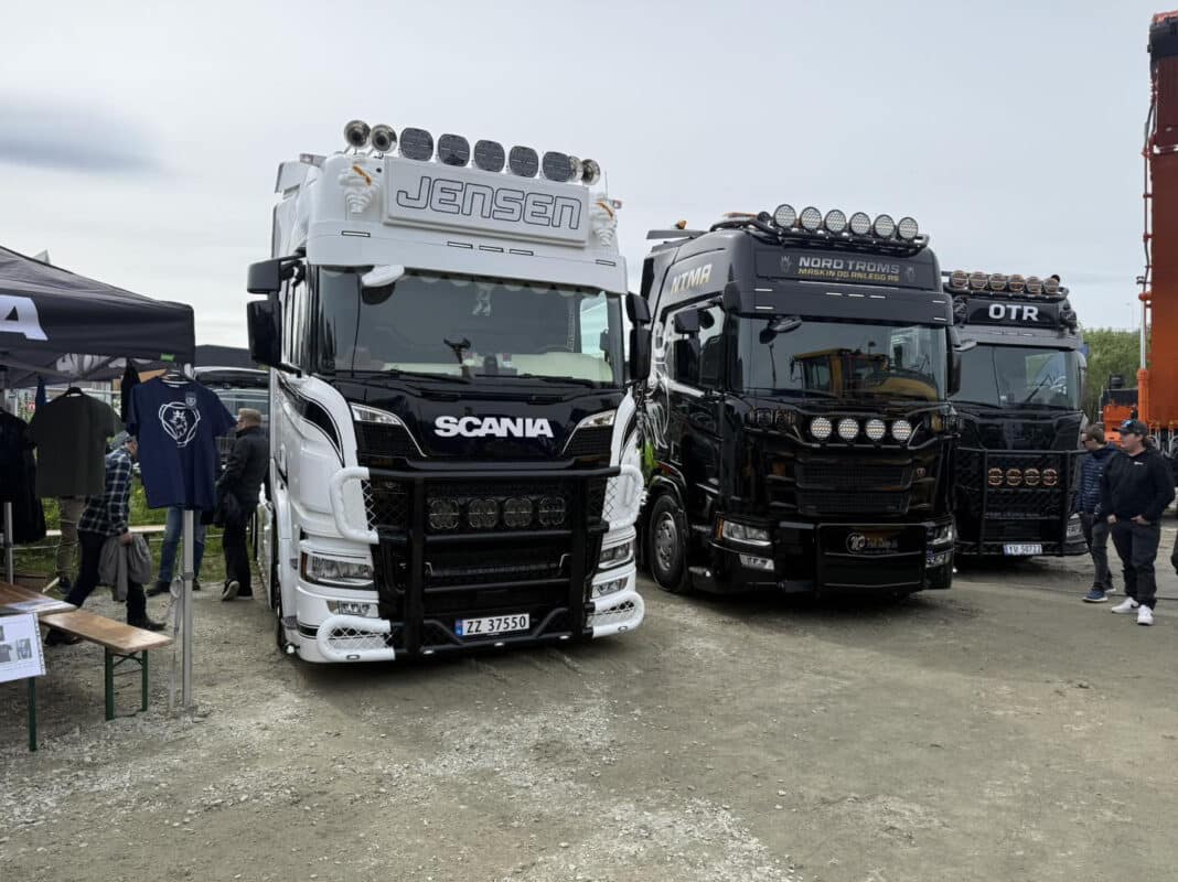 Tre Scania-lastebiler utstilt på et treff, med folk som ser på og snakker ved siden av.